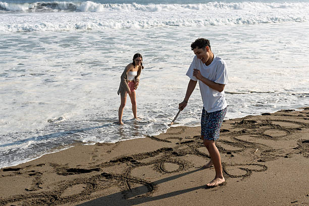 istock Young couple drawing in sand at beach laughing 2252099943
