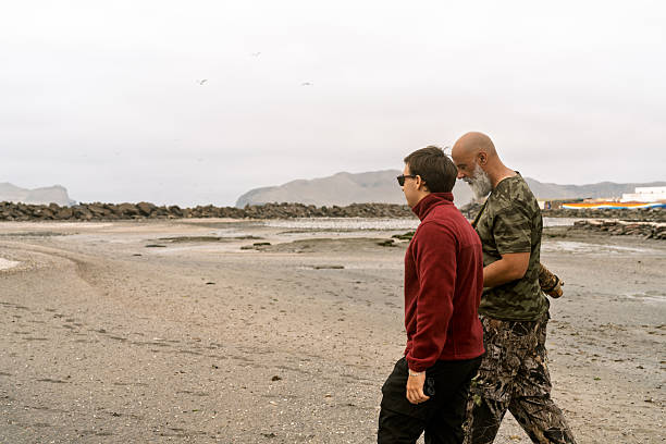 Two men walking on a muddy wetland beach enjoying bird watching. Overcast sky casting a soft natural light