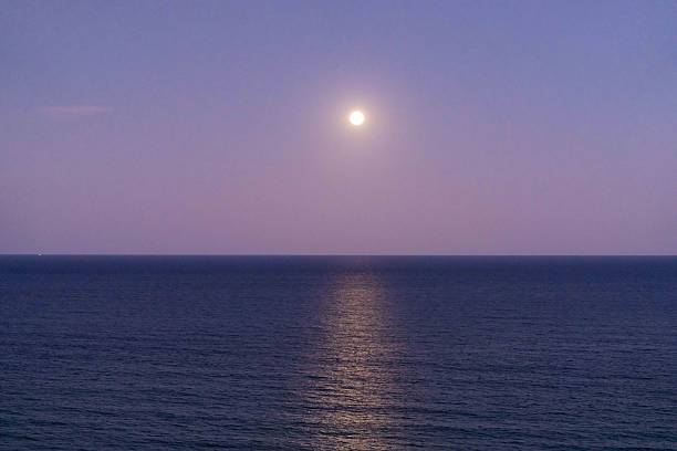 This striking coastal scene captures a bright December supermoon emerging over the ocean at sunset, with warm evening colours reflecting across the water and sky