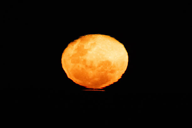 This striking coastal scene captures a bright December supermoon emerging over the ocean at sunset, with warm evening colours reflecting across the water and sky