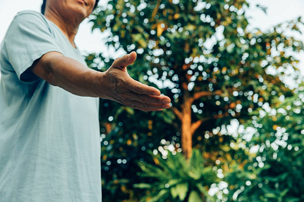 A person stands in a garden with greenery all around. They extend an open hand forward. The sunlight highlights the features of the trees.