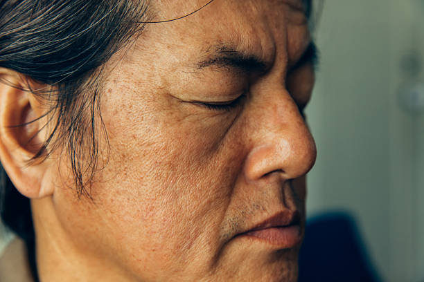 A man sits with his eyes closed, deep in thought. He seems to be reflecting on something meaningful. The setting is simple and indoor. The light softly illuminates his face.