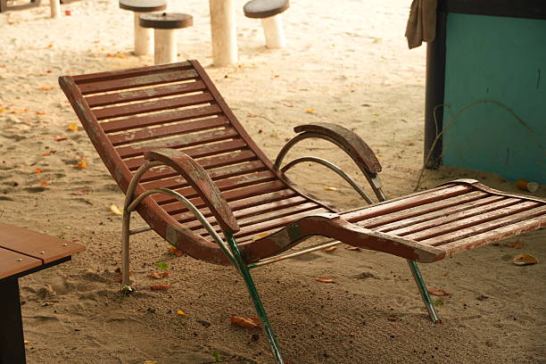 Weathered beach lounge chair on sandy shore with fallen leaves, evoking serene coastal relaxation and tranquility