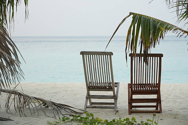 Tranquil beach scene with wooden chairs facing serene ocean view, perfect for relaxation and vacation themes