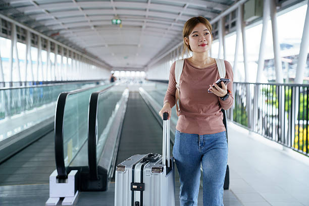 istock Woman using smartphone with suitcase on moving walkway in airport 2252124394