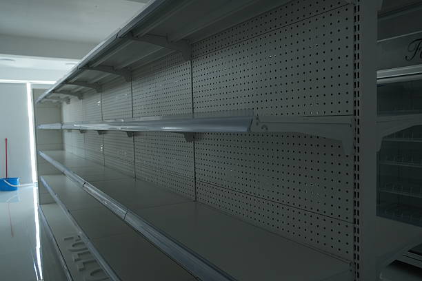 Empty store shelves in a modern retail space with gray metal racks, conveying a sense of scarcity and disruption in commerce.