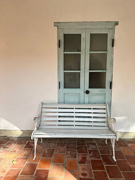 istock A white wrought iron garden bench sits against a white stucco wall next to a pale blue double door with glass panes in a sunny Spanish or Mediterranean style courtyard. 2252131519