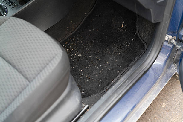 Dirt and small debris cover the floor mat next to the passenger seat in a car.
