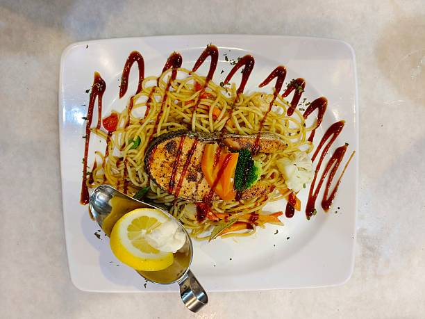 istock Grilled salmon served over stir-fried spaghetti with mixed vegetables, lemon garnish and savory sauce drizzle. 2252134343