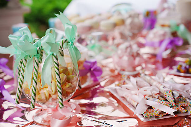 Guests enjoy a table filled with different treats and candies. Items include lollipops, cookies, and chocolates. Bright decorations add fun to the gathering.