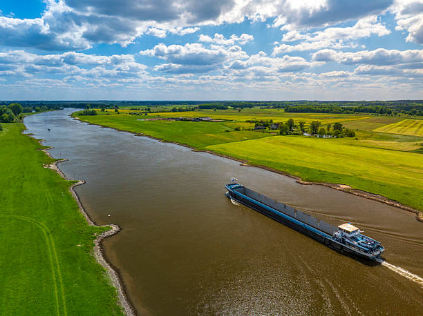 istock Freight ship sailing on the wide Ijssel River, creating a wake as it passes through vibrant green and yellow agricultural fields near Zwolle, Netherlands, on a bright spring day. 2252138323