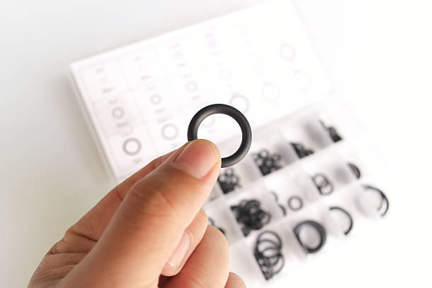 istock A hand holding an O-ring above a clear storage case filled with assorted black rubber gaskets. 2252138453