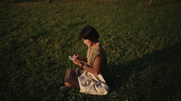 Asian mature woman writing in gratitude journal in nature.