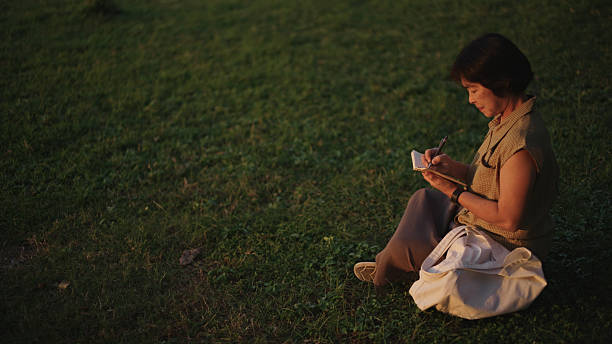 Asian mature woman writing in gratitude journal in nature.