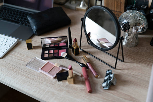 Makeup products are displayed on a wooden desk with a small mirror and a computer nearby.