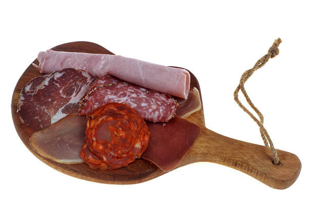 Assortment of deli meats on a wooden cutting board closeup isolated on a white background
