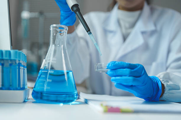 istock Scientist wearing lab coat and gloves performing experiment by dropping blue liquid from pipette into petri dish in modern laboratory with test tubes and beaker 2252144310