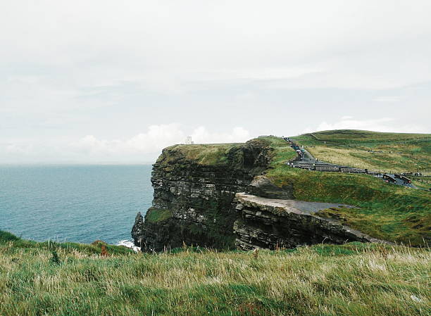 Green Cliffs of Moher in Ireland, County Clare. The day is sunny. Tourists are seen.