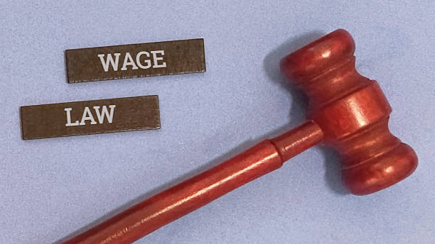 istock Wage law concept represented by small wooden blocks labeled wage and law alongside a miniature red judge's gavel resting on a light blue textured surface. 2252146151