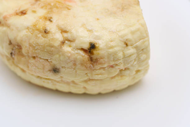 A piece of spoiled cheese is shown on a white plate. The surface is covered with mold, indicating it is no longer fresh or safe to eat.