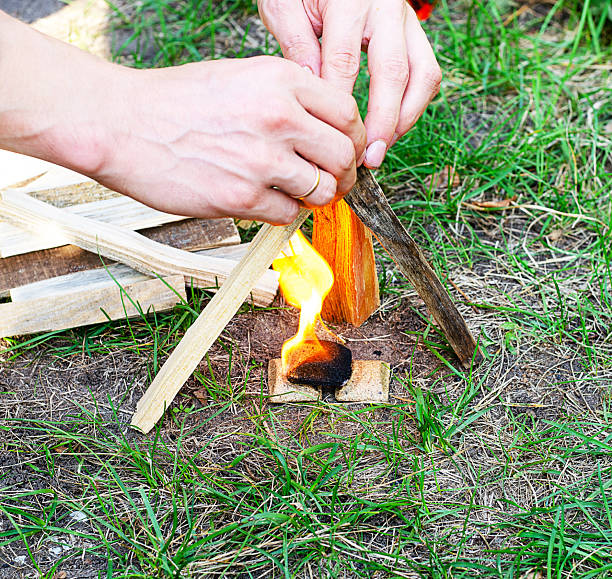 Hands lighting a small campfire with kindling and tinder on the grass