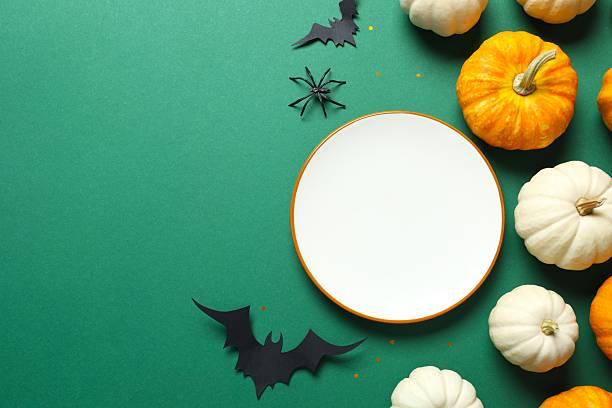 istock Halloween table with white plate, pumpkins, bats and spiders on color background 2252152099