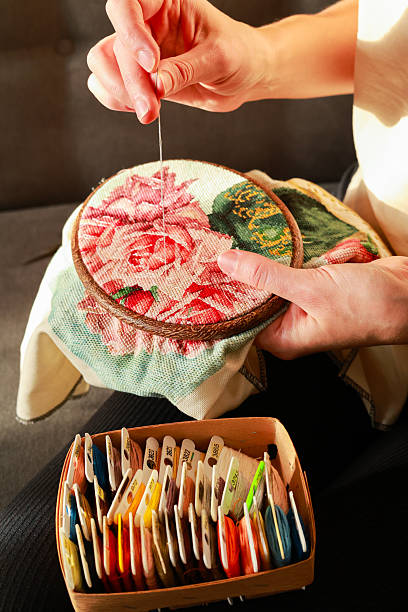Close-up of embroidery hoop with white canvas, two sewing needles and green threads arranged for cross-stitch project concept of craft