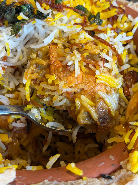 istock Image of spoon serving saffron-yellow chicken biryani rice from a terracotta pot, accompanied by naan and parathas, garnished with green chillies 2252155103