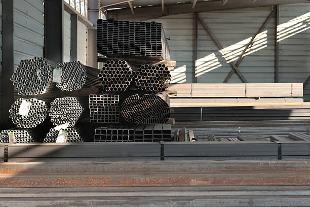 Wide view of stacked square and rectangular steel hollow section profiles with labels stored inside an industrial metal warehouse.