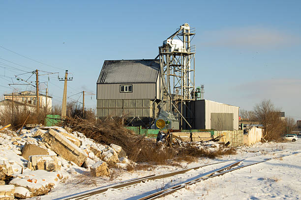 A wide-angle shot of a corrugated metal industrial building and a tall grain elevator structure set against a clear blue winter sky