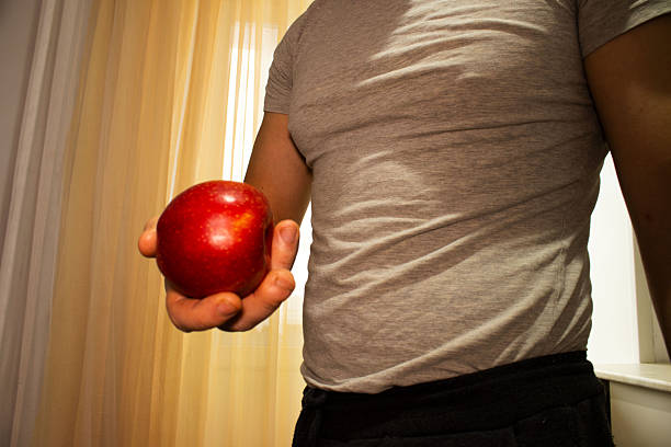 A medium close-up shot of a man in a grey t-shirt holding a vibrant, shiny red apple in his hand