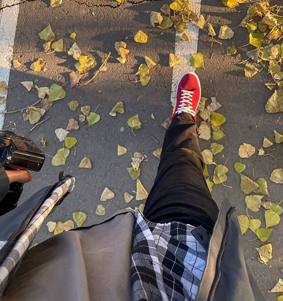 A man captures the beauty of autumn leaves while strolling on a quiet pathway