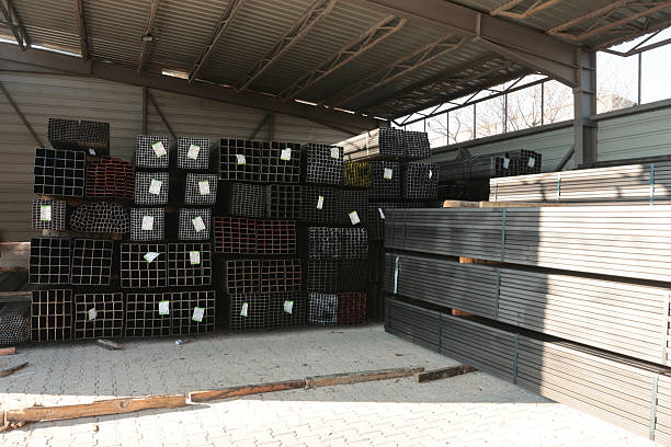 Wide view of stacked square and rectangular steel hollow section profiles with labels stored inside an industrial metal warehouse.