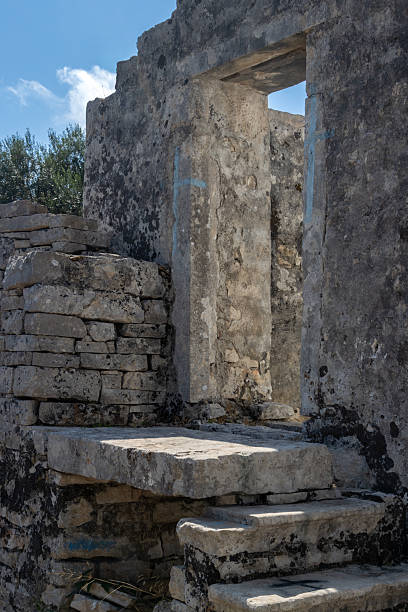 Abandoned part of a church. Stone building with stairs. Blue painted crosses on the doorway. Blue sky with white clouds. Makratika, Paxos, Greece.