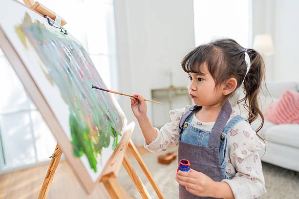 istock Child paints on canvas while standing in a well-lit room with a cozy sofa in the background during daytime 2252179612