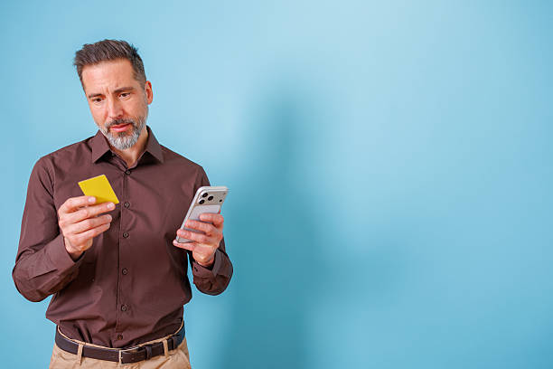 istock Middle-aged man focused on his smartphone and credit card, appearing anxious while shopping online 2252180628