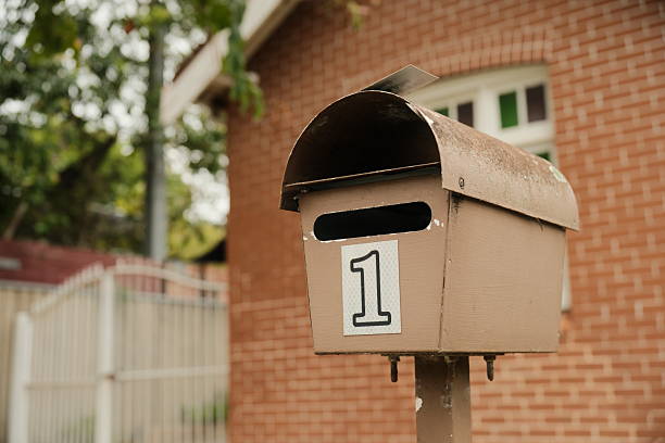 Brown metal mailbox on a pole with a brick house behind.