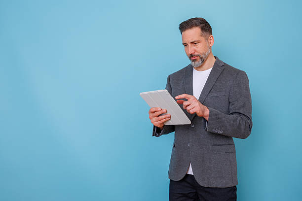 istock Mature adult man using digital tablet for business communication and remote work on blue background with copy space 2252184425