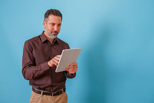istock Mature adult man browsing digital tablet, using touch screen technology for business communication on blue background 2252185199