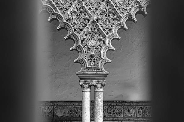 Black and white photograph of an ornate Moorish arch supported by carved stone columns, showcasing intricate Islamic geometric patterns and fine architectural craftsmanship. A timeless architectural detail ideal for fine art, heritage, and design-focused visual projects.