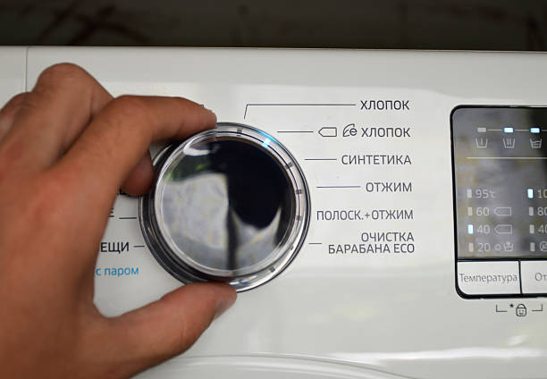 Tiraspol, Moldova - June 25, 2023: A hand turning the wheel of a washing machine - labels (cotton, synthetics, spin, spin) are visible nearby, and a display with indicators is visible on the right.