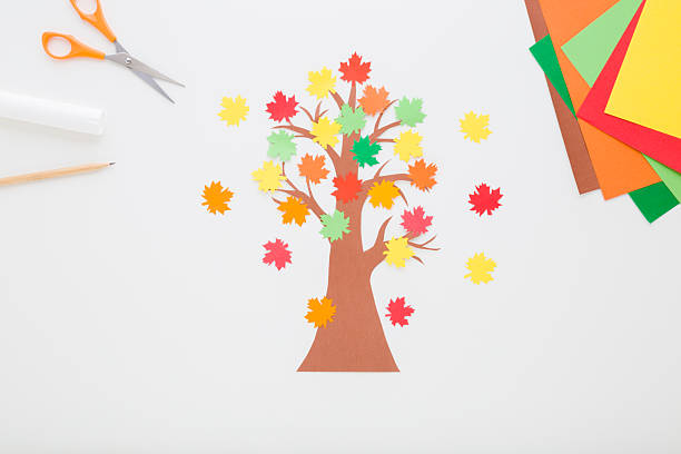 istock Created brown tree with colorful maple leaves from application paper on light gray table background. Closeup. Making autumn decoration. Child handcraft. Top down view. 2252190172