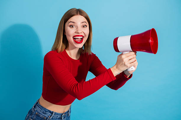 istock Charming young woman holding a red megaphone against a blue background, expressing confidence and energy in a casual outfit 2252191364