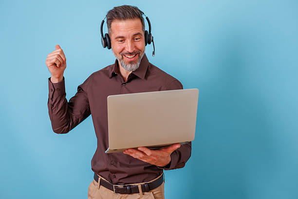 istock Happy man wearing a headset with microphone, holding a laptop and gesturing while having an online video call 2252192331
