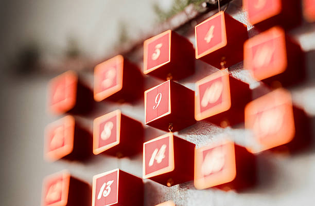 A close-up of glowing red advent calendar cubes numbered in a cascading grid, creating a warm, festive countdown scene with soft focus and bokeh.
