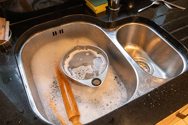istock Black granite worktop with stainless steel sink filled with soapy water containing baking utensils that are to be washed. 2252204203
