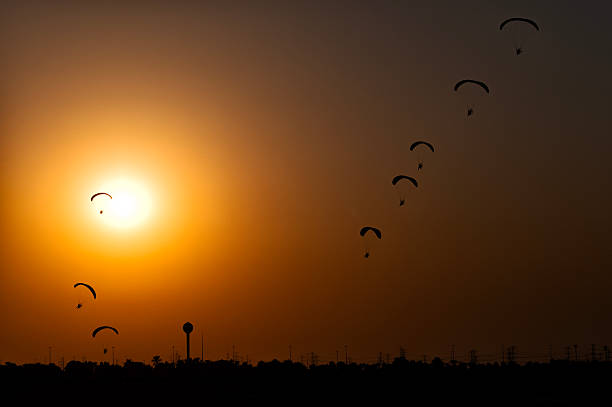 Paramotor pilots approaching the airfield for landing together in formation at sunset.