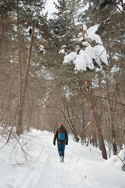 Smiling mid adult woman in big green knit hat and sport jacket enjoys fresh air at walk in forest surrounded by snowy landscape