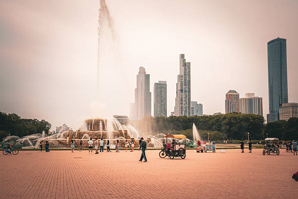 Buckingham Fountain spraying high against the modern Chicago skyline on a summer day. People enjoying the park and city life around the iconic landmark.