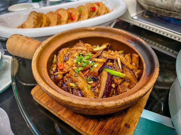 A mouthwatering clay pot dish featuring succulent pork slices and tender eggplant, bathed in savory sauce, on a table setting that highlights inviting flavors and textures. Chinese food